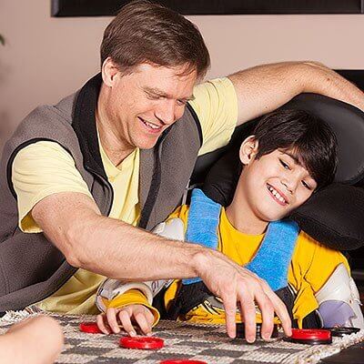Boy with a disability in a wheelchair playing checkers with father at home